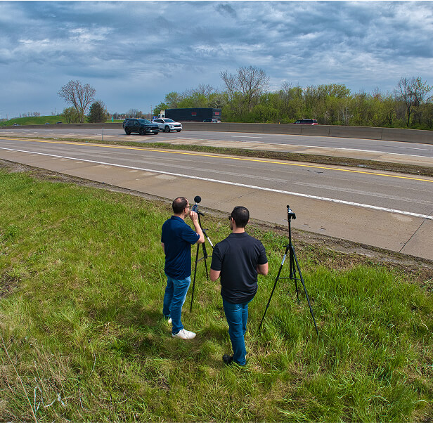 Two men testing noise outdoors with decibel meter microphones.