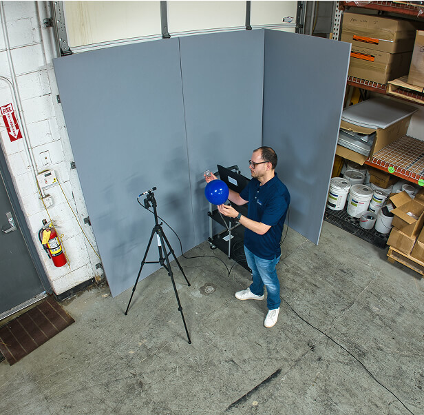 An employee of Memtech Acoustical testing popping a balloon in an area with acoustic pads towards a mic.