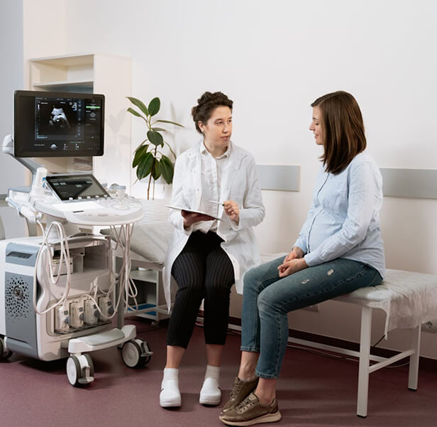 A female doctor talking to a pregnant woman and there is an ultrasound machine.