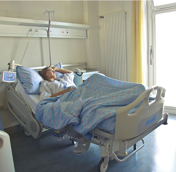 A woman staring outside the window while lying on a hospital bed.