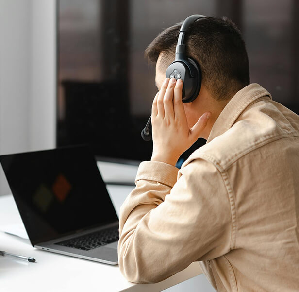 An agent wearing a headphone while looking at his laptop.