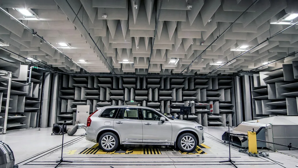 Inside an anechoic chamber during vehicle acoustic testing, with sound-absorbing wedges lining the walls and engineers measuring noise emissions.