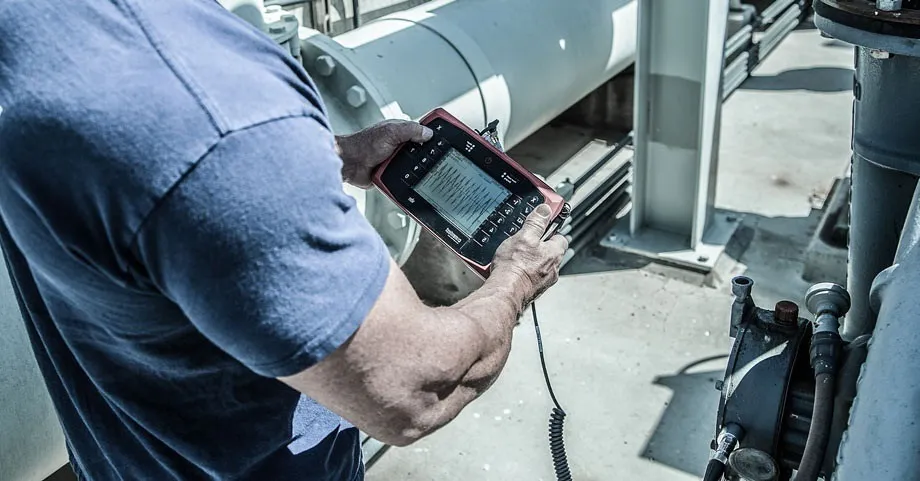 Over-the-shoulder view of an engineer using a handheld instrument to perform industrial vibration analysis on mechanical equipment.