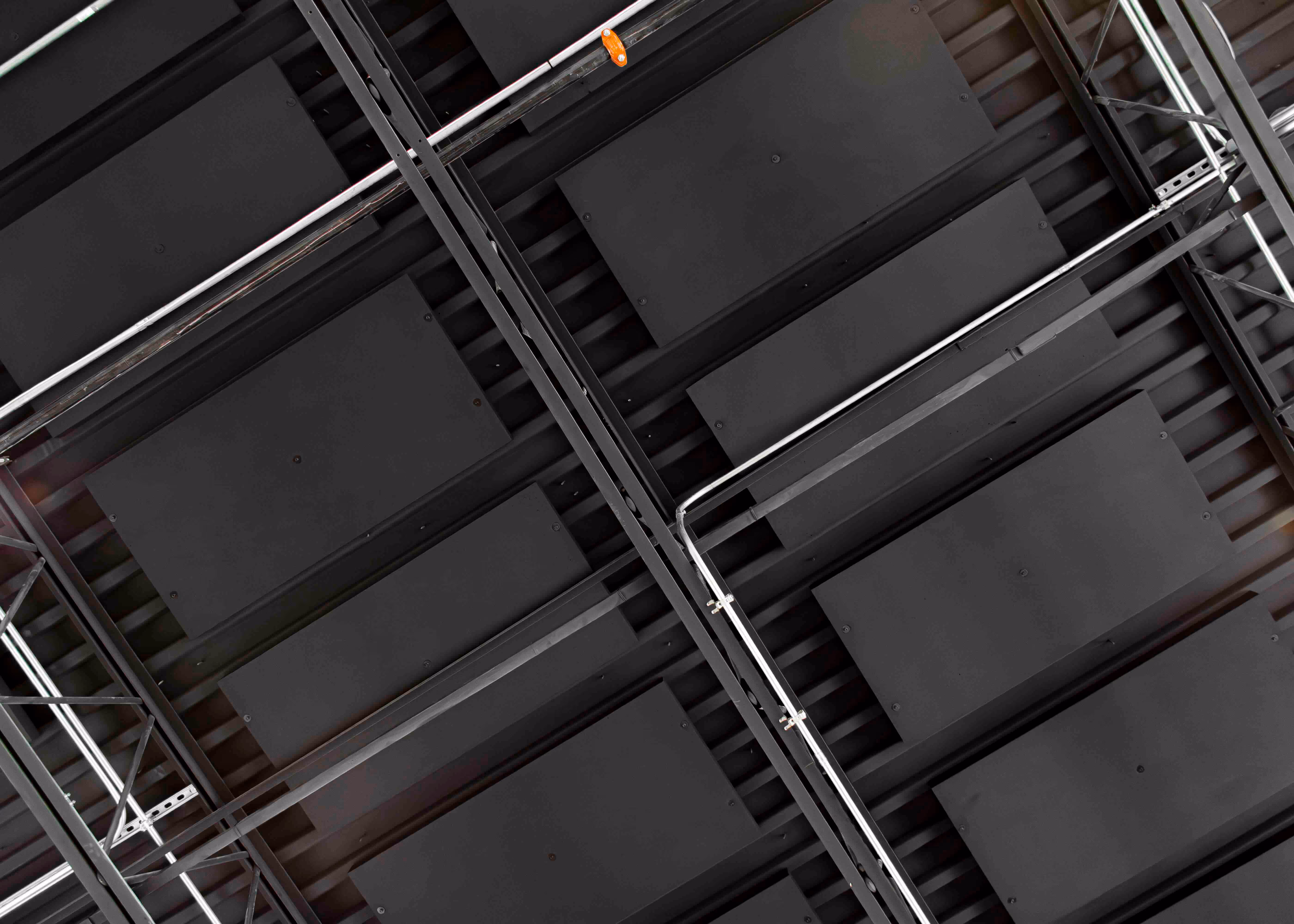 Close-up view of a black open ceiling with mounted acoustic panels and exposed metal conduit in a commercial or industrial space