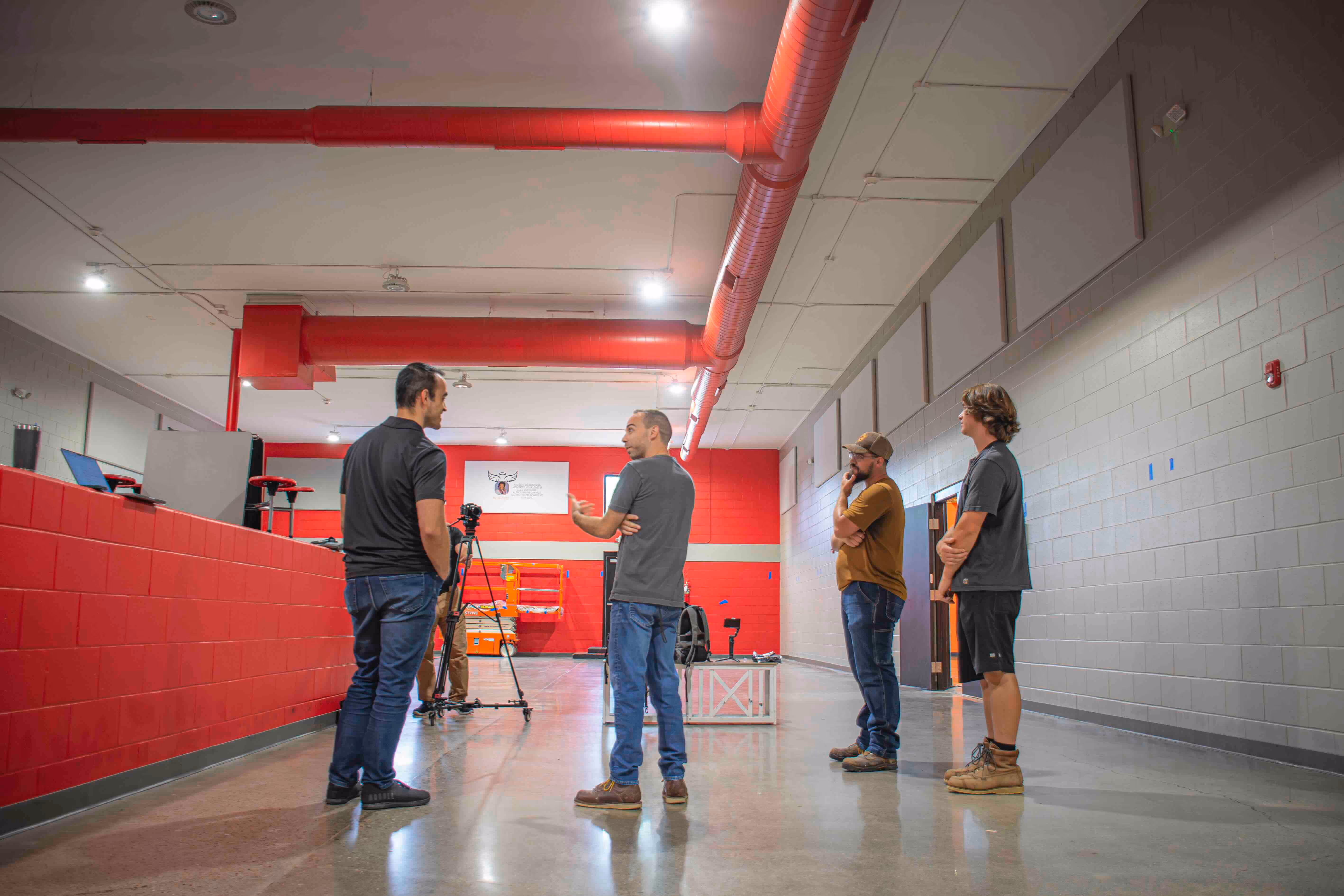Technician in blue uniform installing acoustic panels on a ceiling using a lift in an industrial building.

