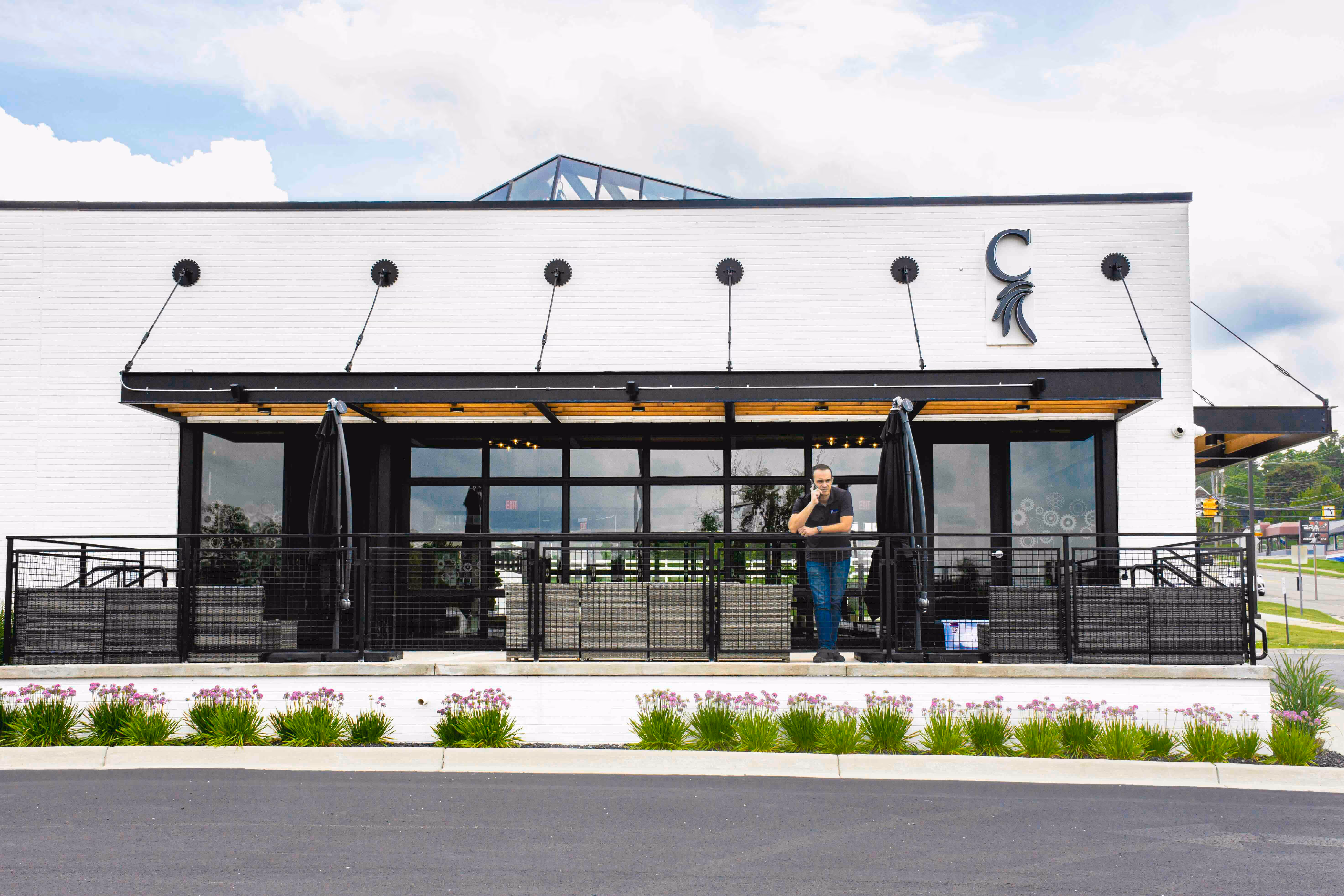 Exterior view of a modern white brick commercial building with large black-framed windows and a patio, featuring a man on the phone and the Memtech Acoustical logo on the facade.