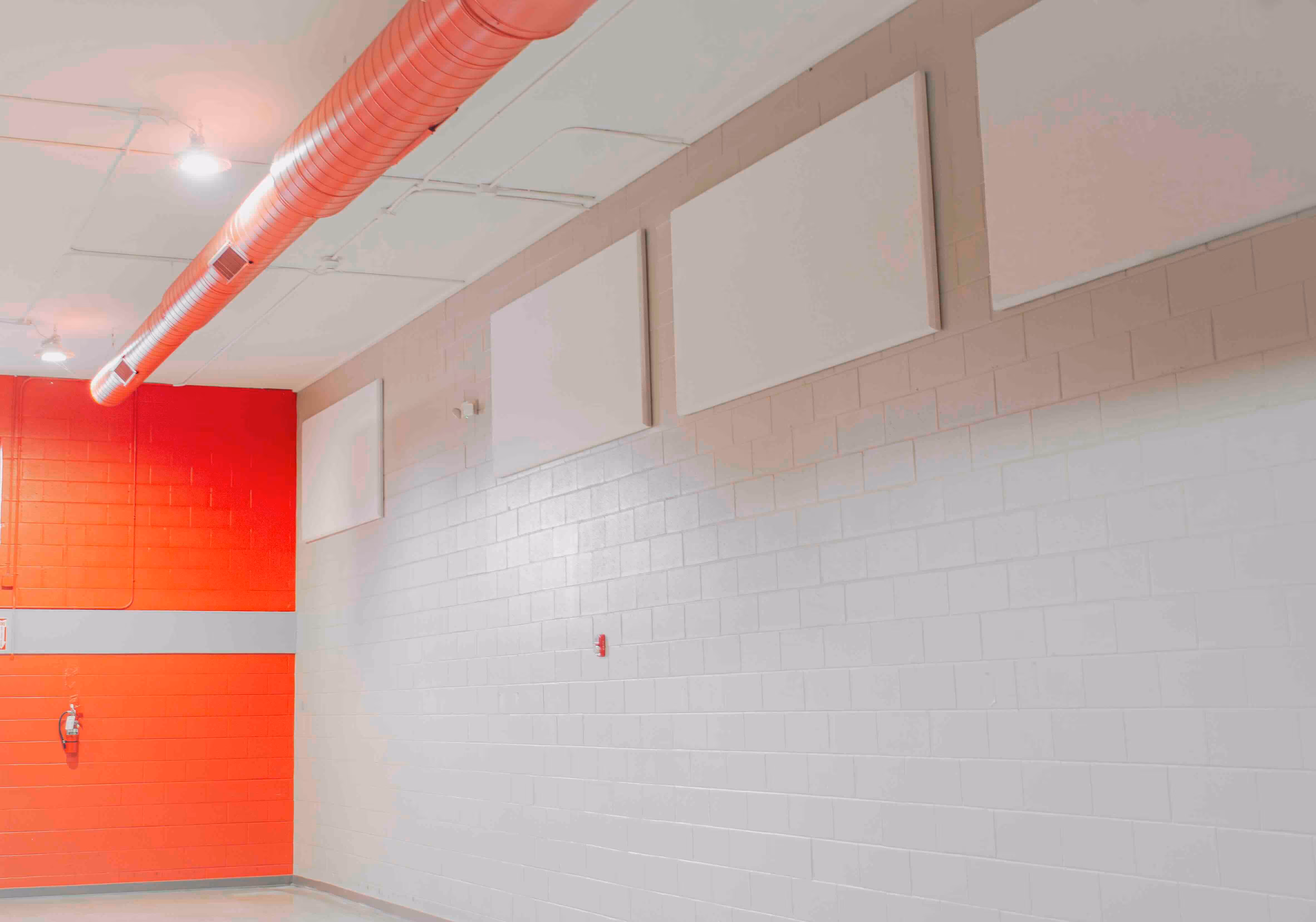 Interior wall with a red and white color scheme, featuring rectangular acoustic panels and exposed ceiling ductwork