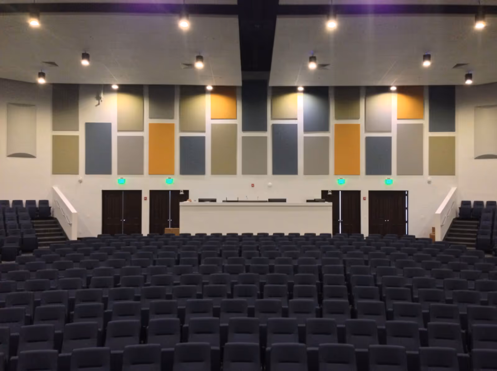 Interior of a modern auditorium with tiered seating and colorful acoustic wall panels for sound absorption and improved audio clarity