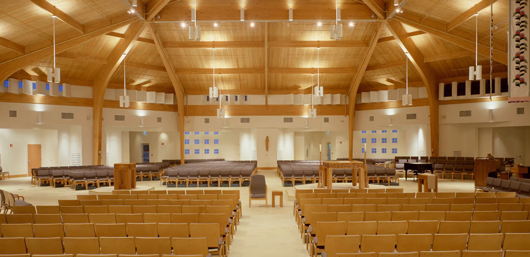 Spacious church interior with wooden vaulted ceiling, modern lighting, and rows of seating facing the altar area.