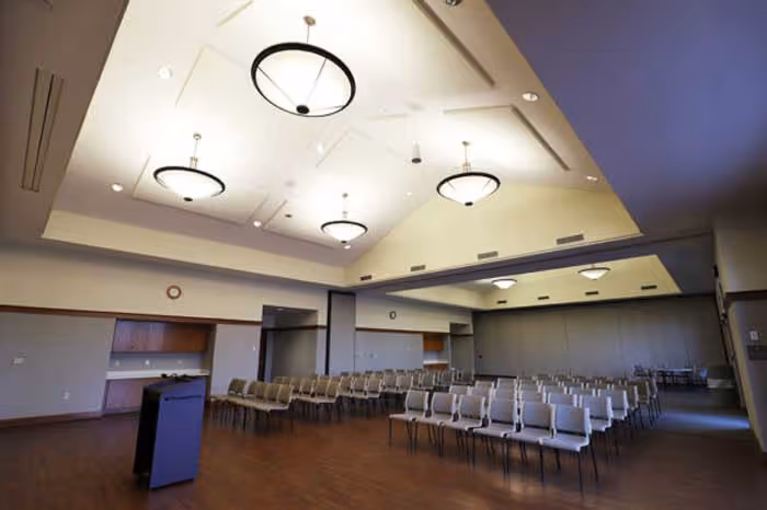 Conference or event room with rows of chairs, a podium, and high ceilings with modern lighting fixtures.