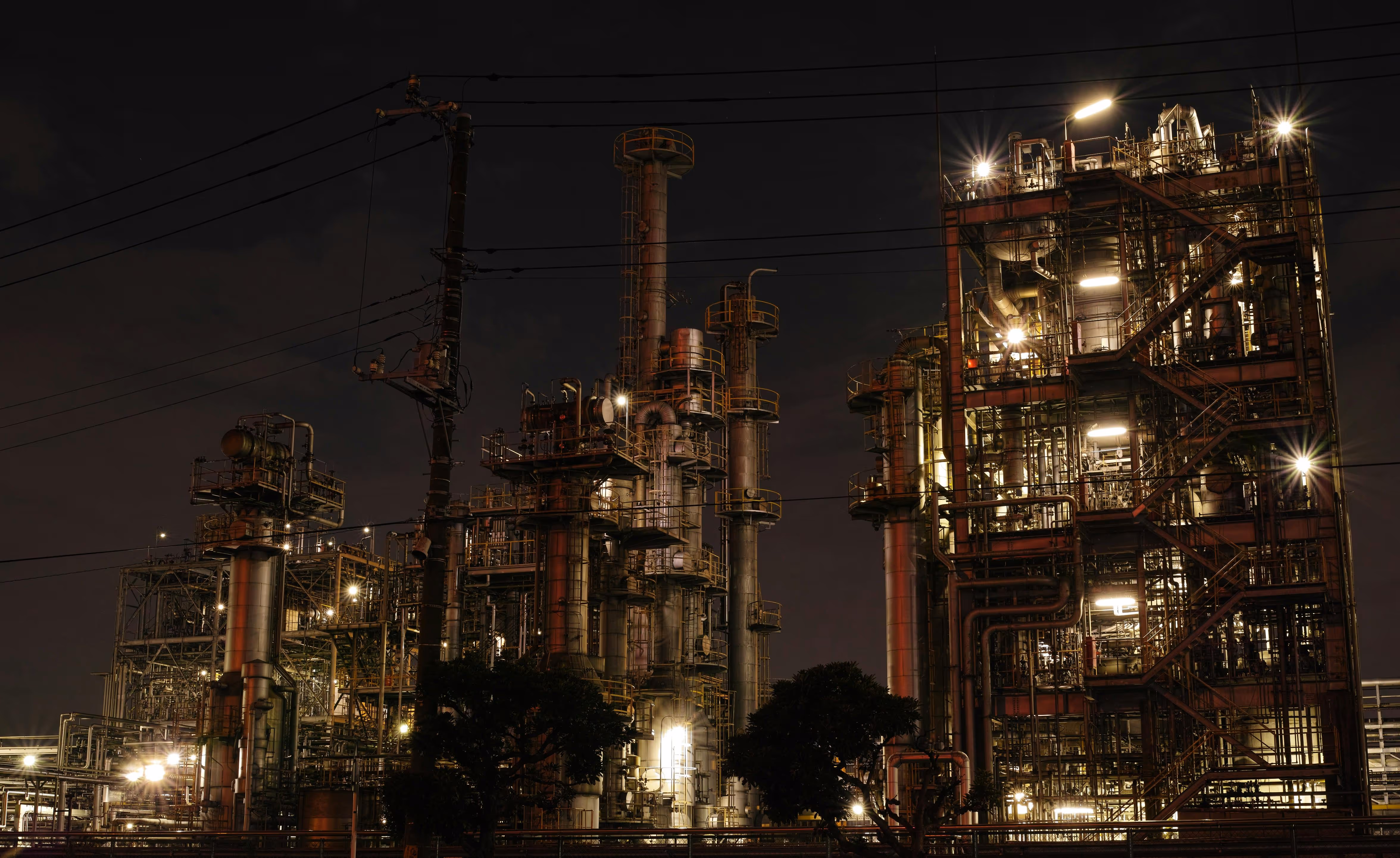 Industrial refinery complex illuminated at night, with multiple towers, pipes, and structural frameworks.
