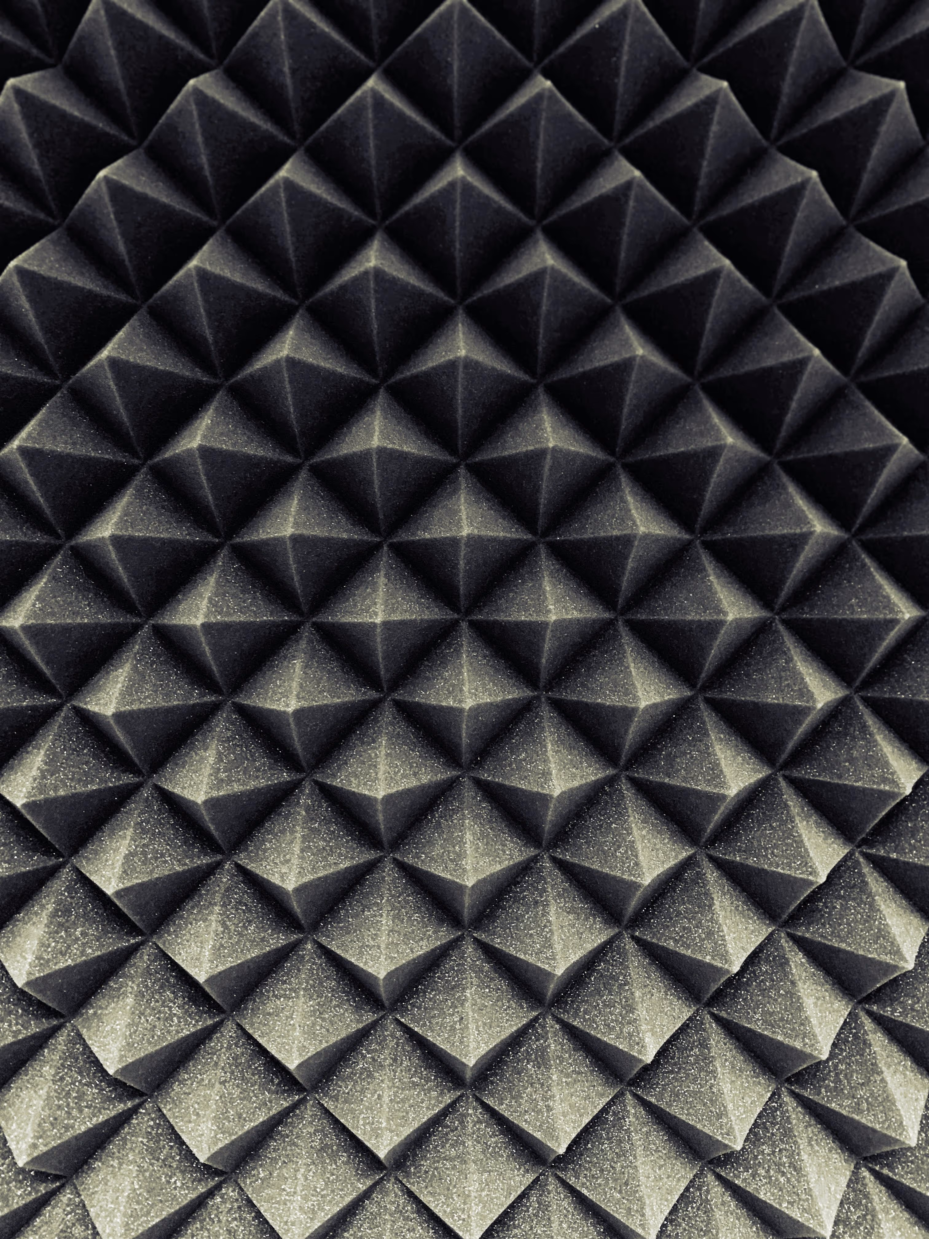 Close-up of dark gray acoustic foam panels with pyramid-shaped protrusions arranged in a grid pattern.