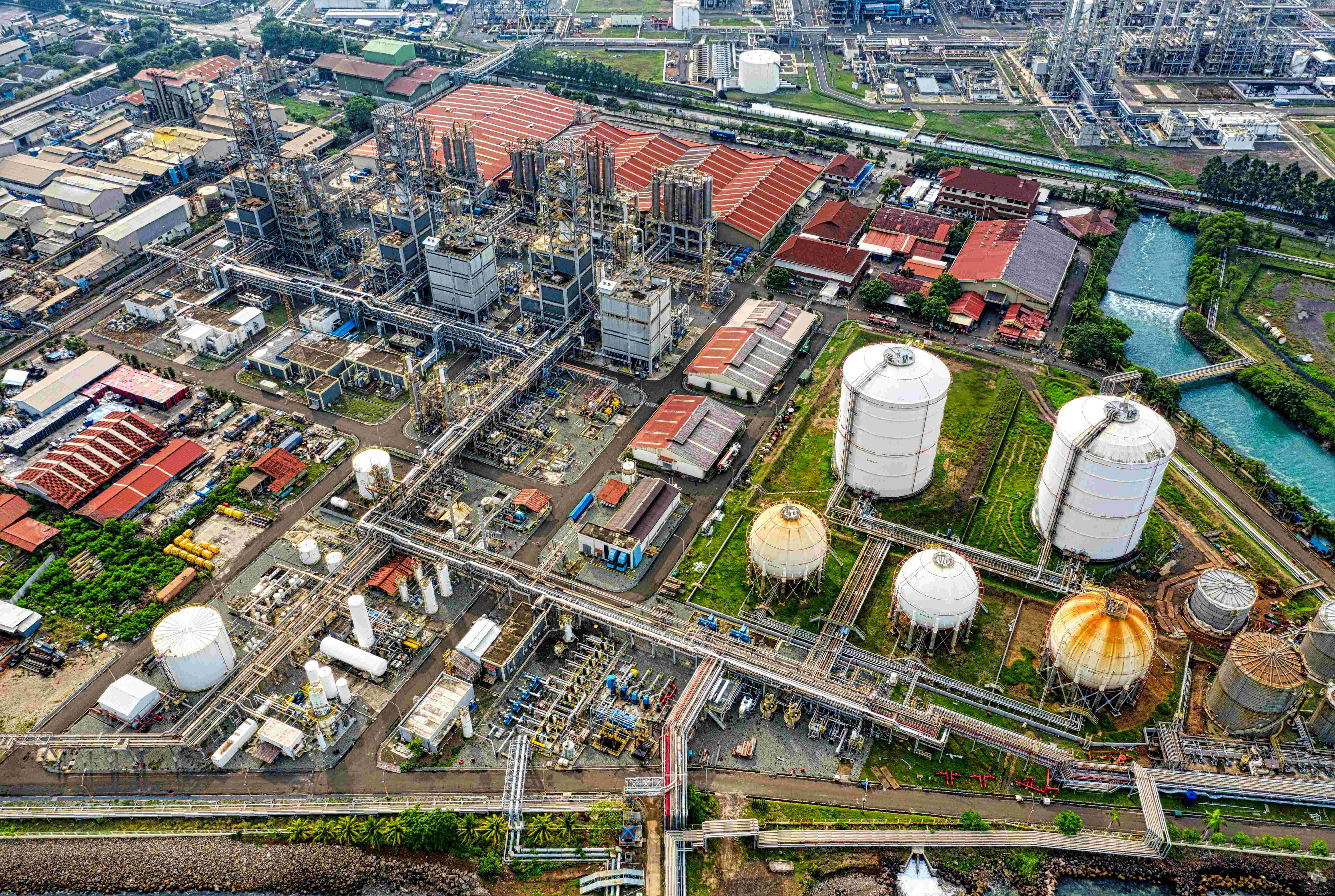Aerial view of a large industrial refinery complex with storage tanks, processing units, and surrounding infrastructure.