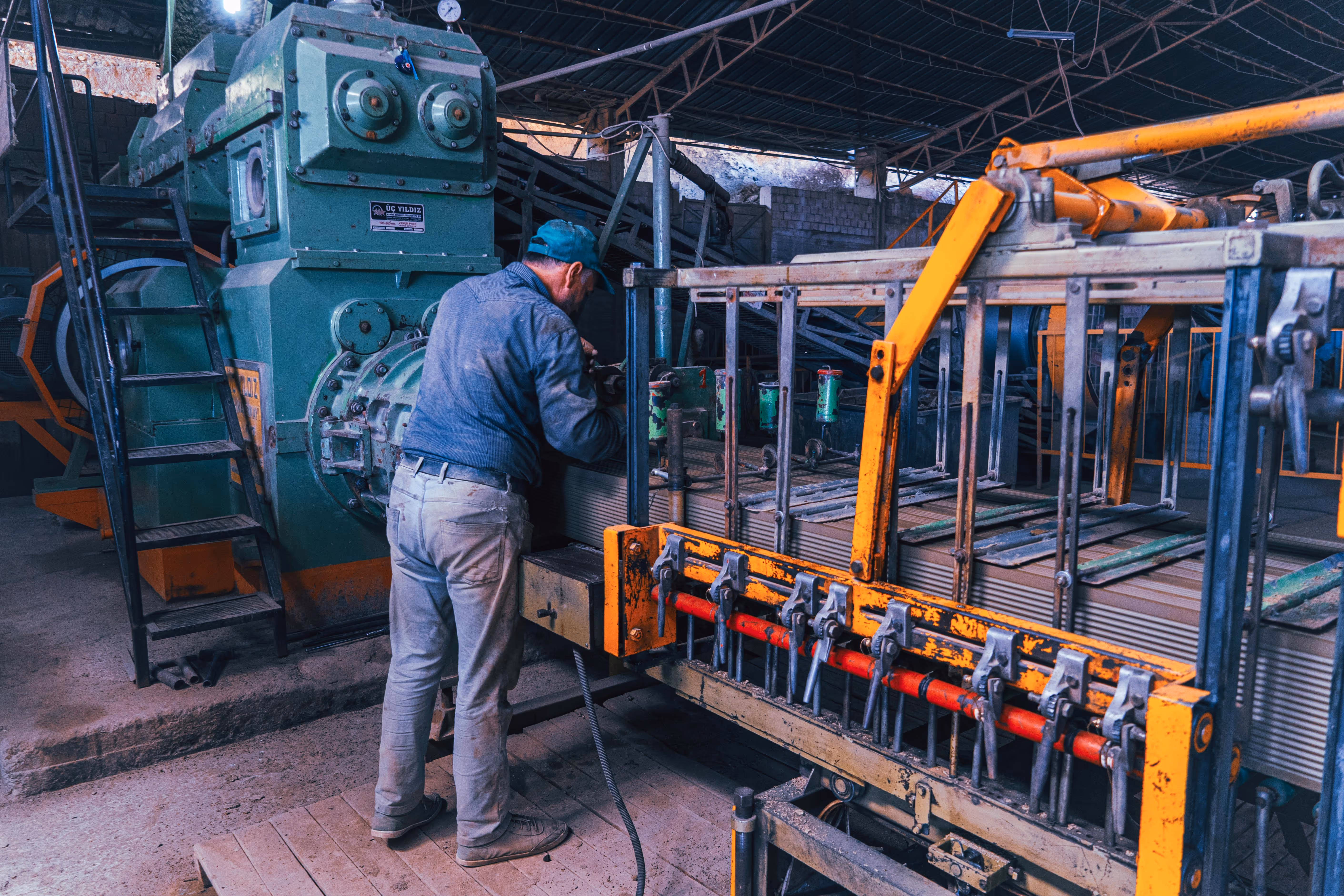 Technician operating industrial machinery in a factory setting, surrounded by heavy equipment and control systems.