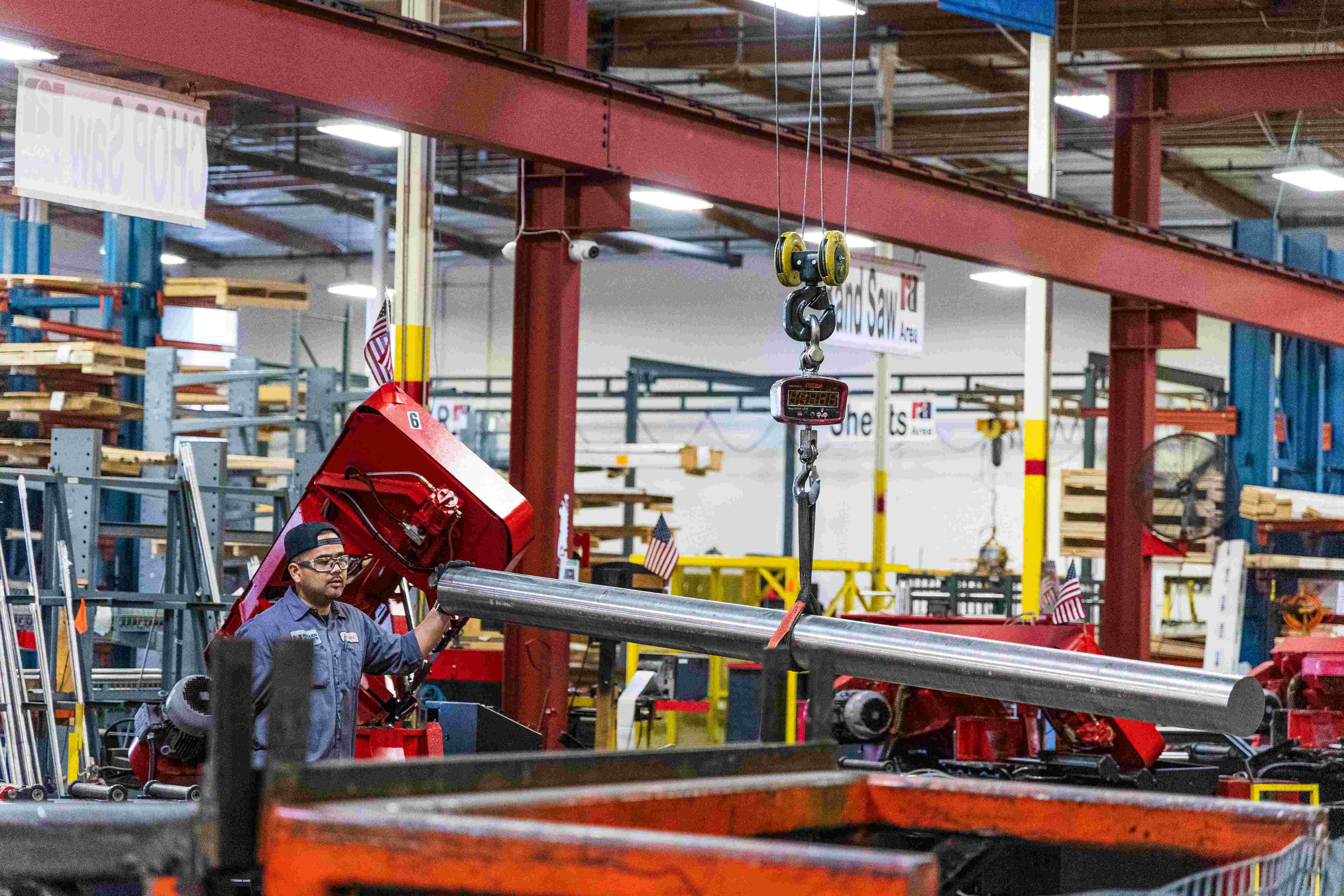 Factory worker operating machinery to cut or shape a long metal beam inside an industrial manufacturing facility.
