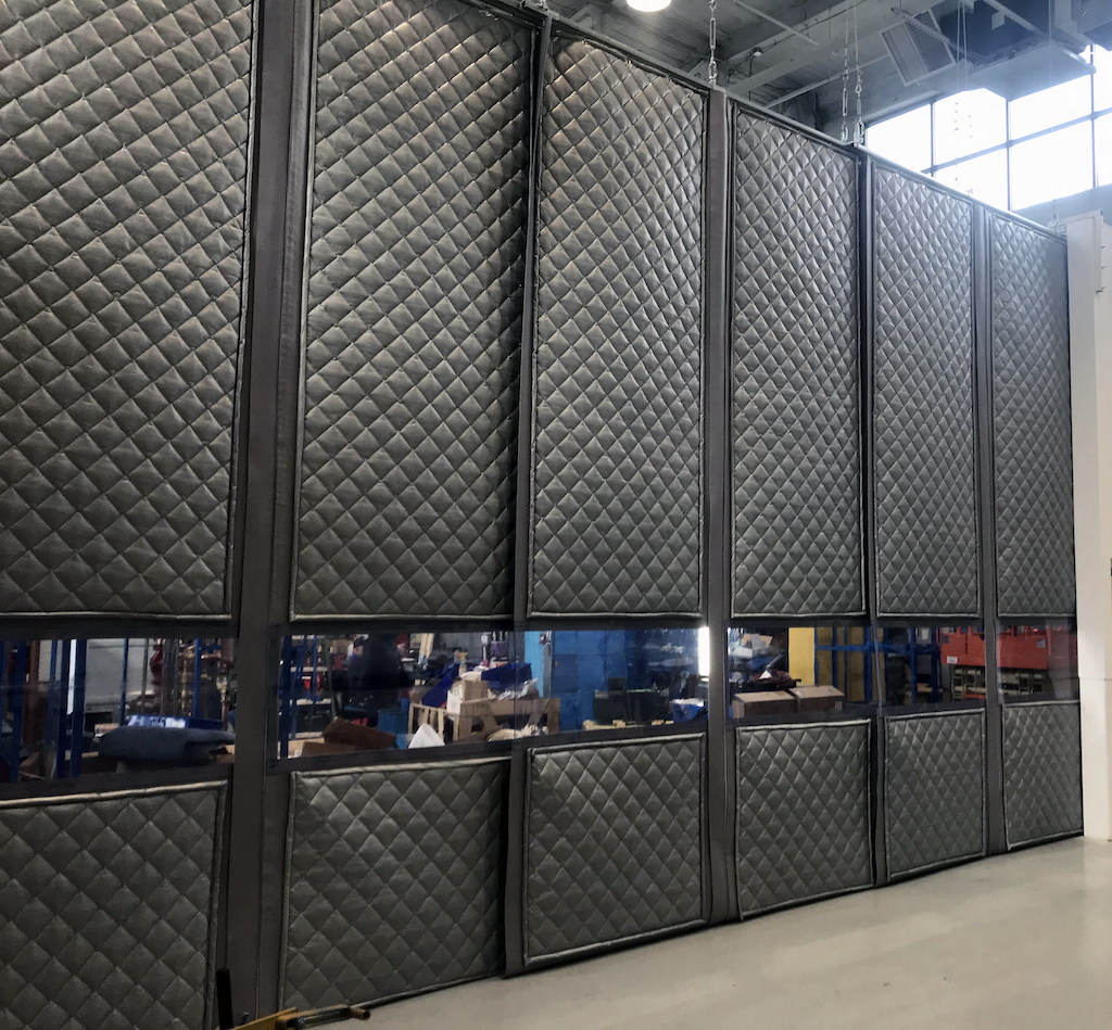 Industrial sound curtain enclosure with quilted acoustic panels used to isolate loud machinery and reduce workplace noise levels.