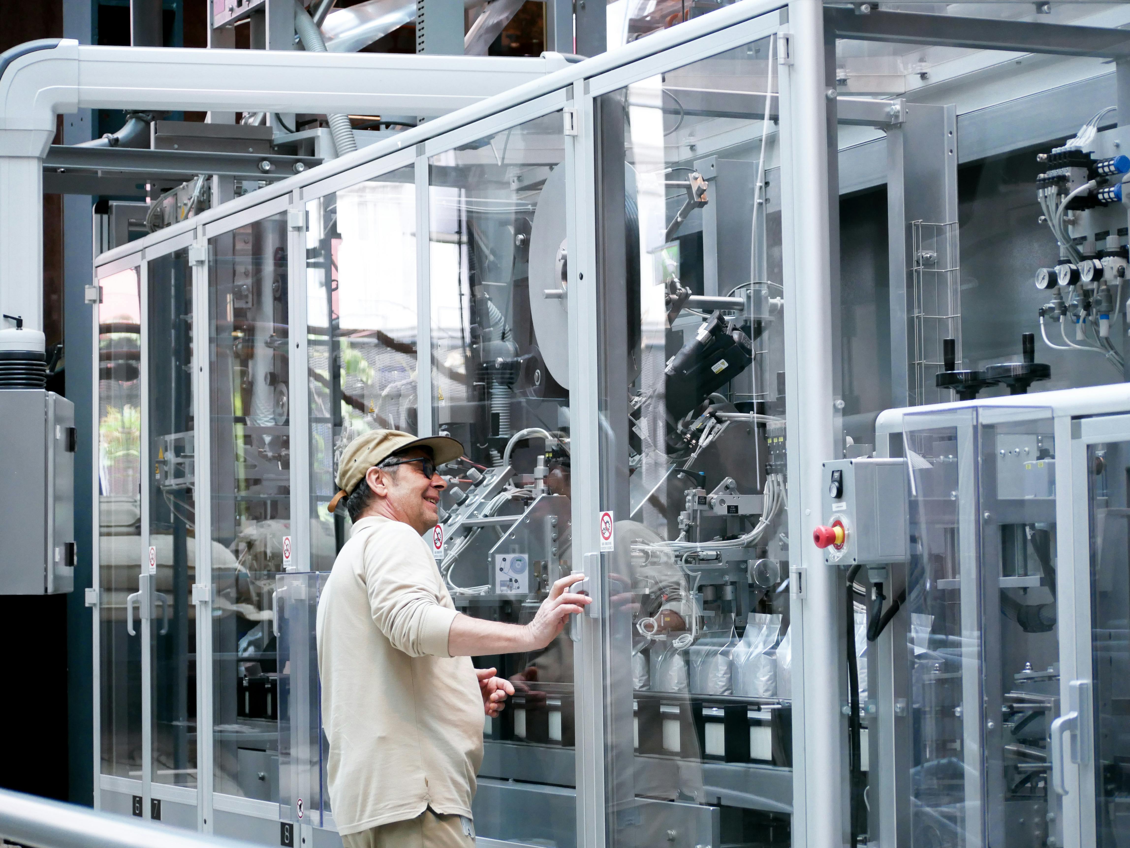 Technician operating machinery behind a transparent industrial noise enclosure designed for acoustic safety and equipment access.