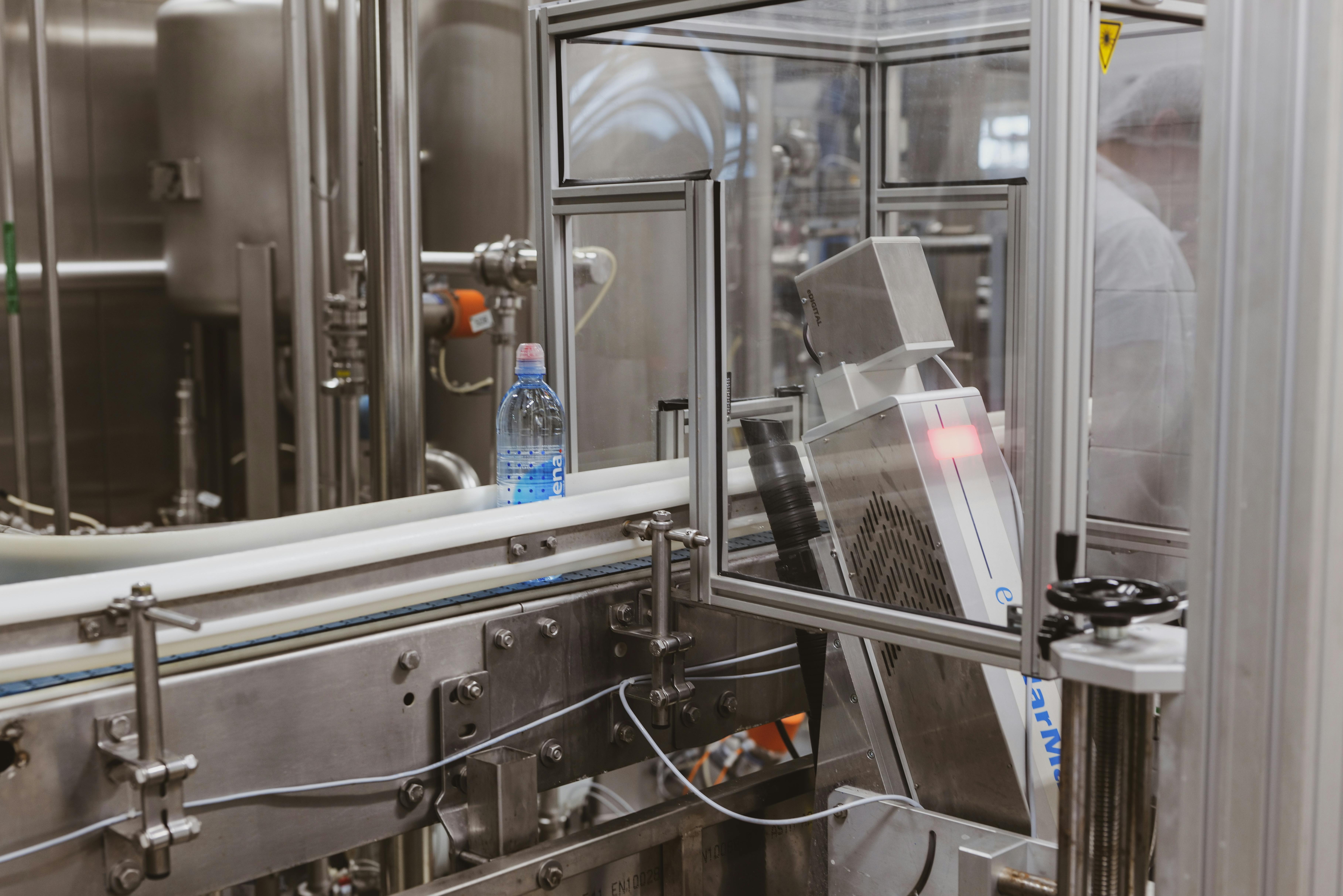 Bottling line inside an industrial facility with transparent acoustic enclosures for machinery noise control and operator safety.