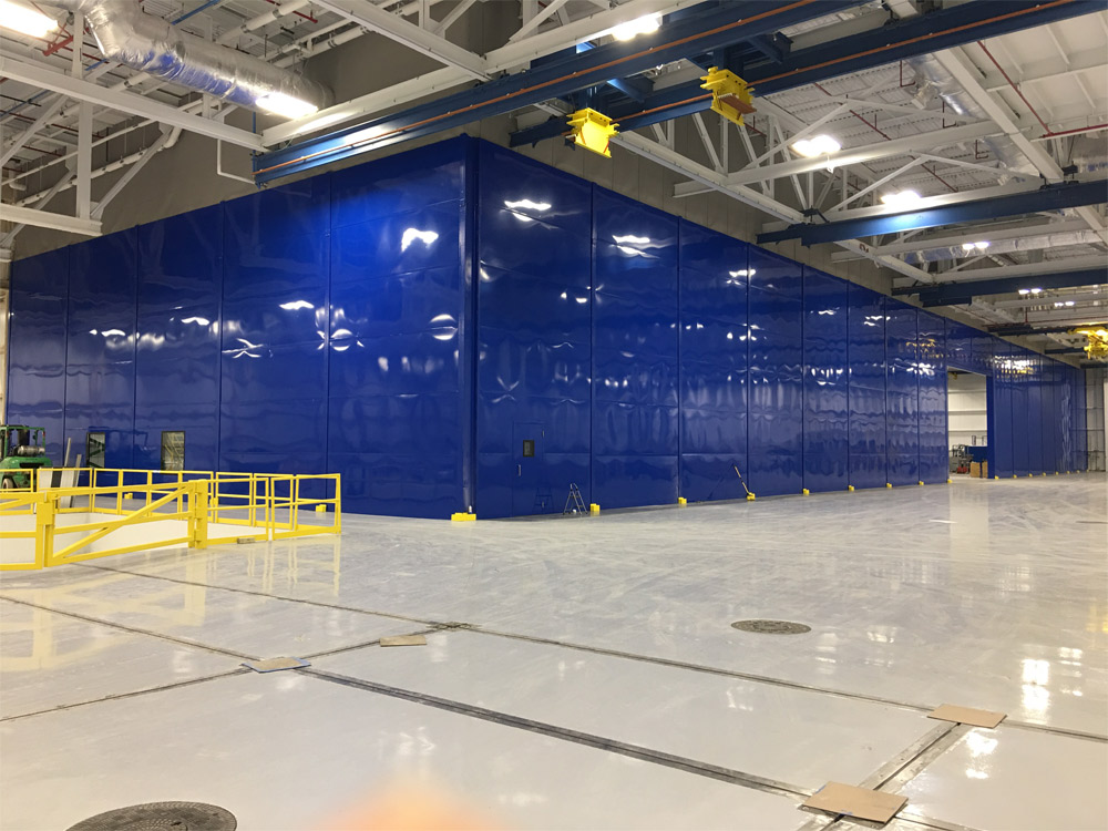 Large industrial acoustic enclosure with high-gloss blue sound curtain panels used to contain noise in a factory environment.