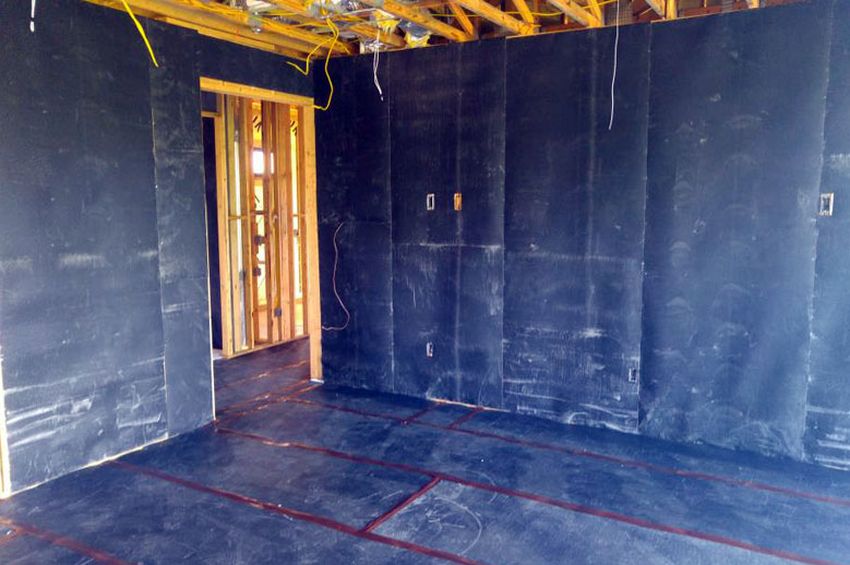 Interior view of a construction site with mass loaded vinyl (MLV) barrier applied to walls and floor for soundproofing and noise control.