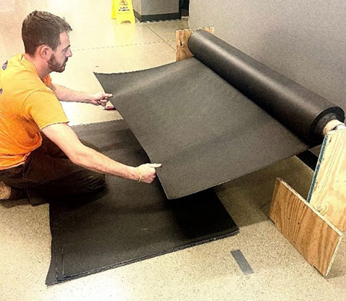 Technician unrolling a sheet of mass loaded vinyl (MLV) sound barrier for acoustic treatment or soundproofing installation.