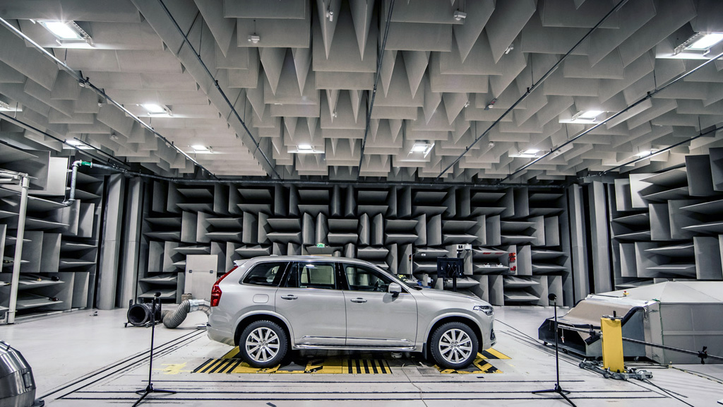 Silver car inside an anechoic chamber with wedge-shaped acoustic panels on all surfaces, used for precise vehicle noise and vibration testing.
