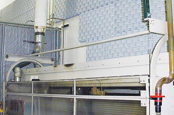 Industrial machine with quilted acoustic blankets lining the surrounding walls for noise control in a manufacturing environment.