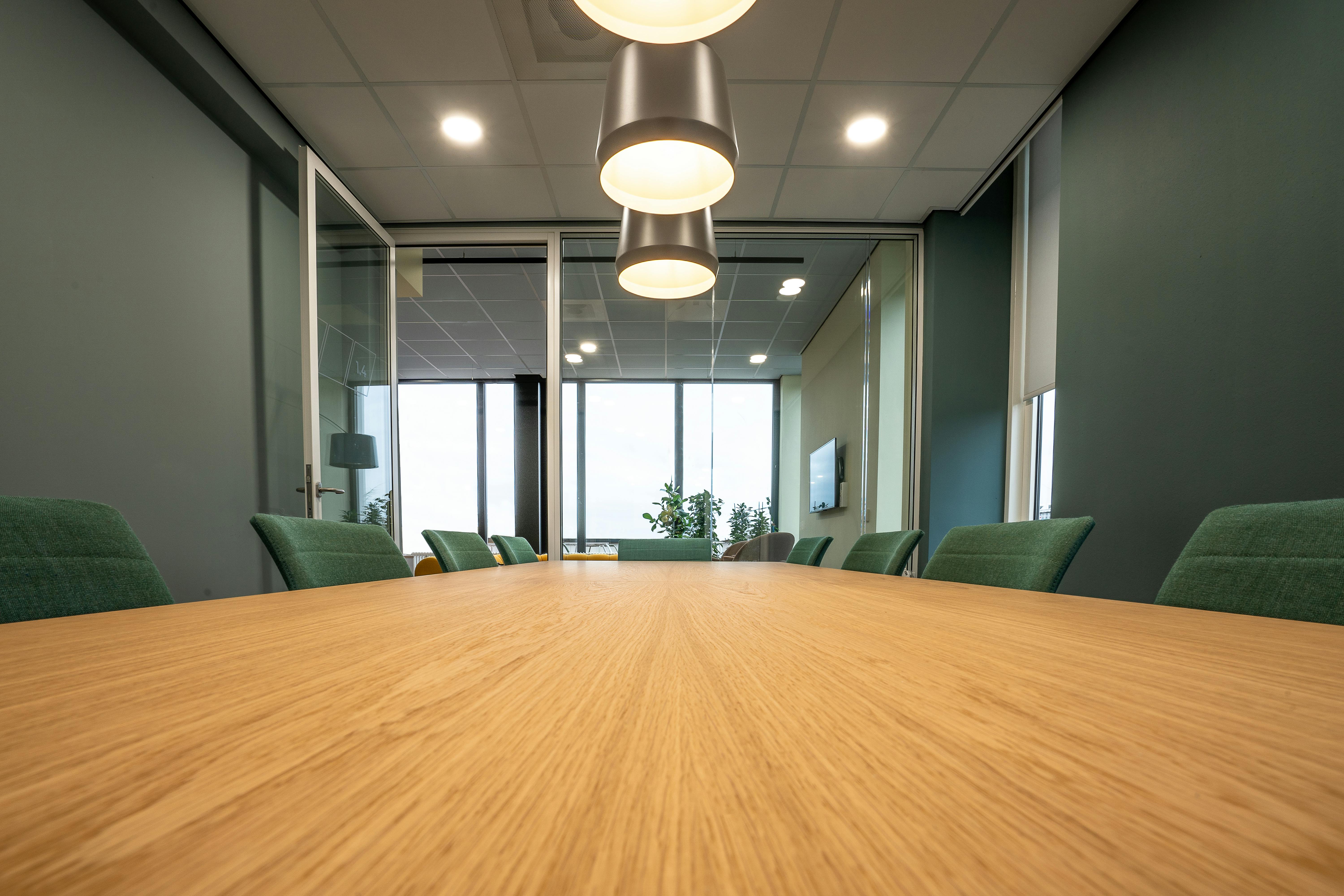 Modern conference room with acoustic ceiling tiles and green upholstered chairs, designed for speech clarity and sound absorption.