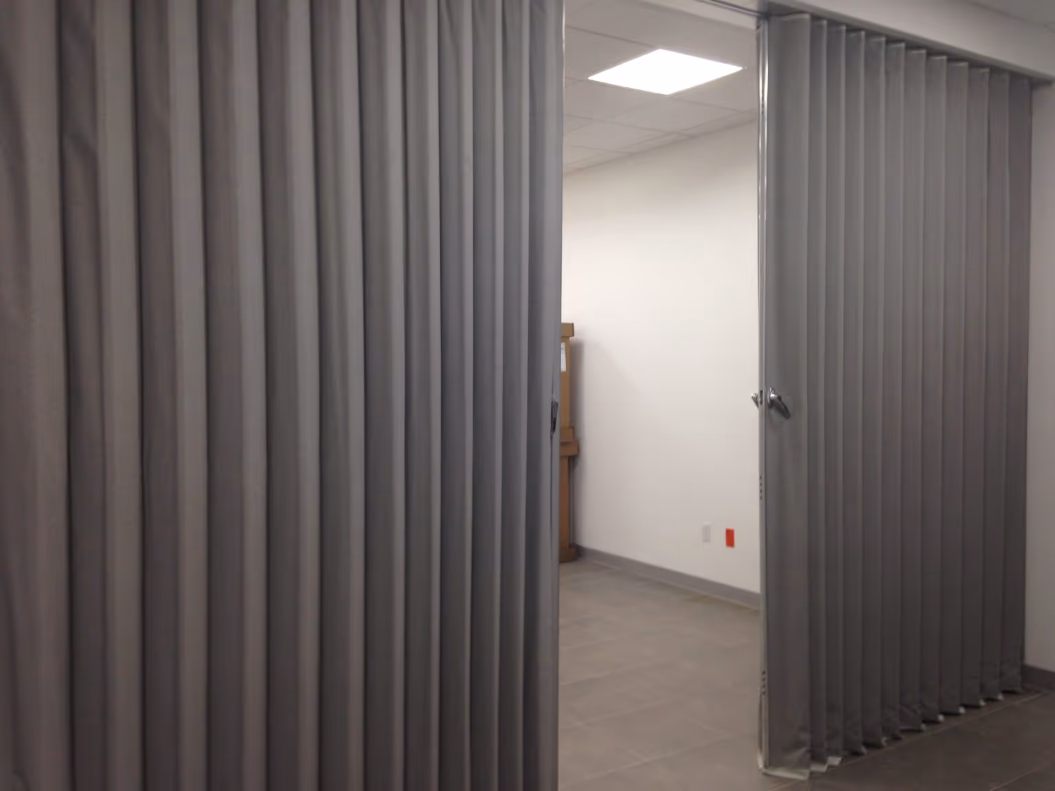 Partially open gray bi-part accordion room divider in a tiled modern indoor space.