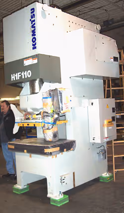 Large Komatsu H1F110 industrial machine in a factory setting with two people in the background.