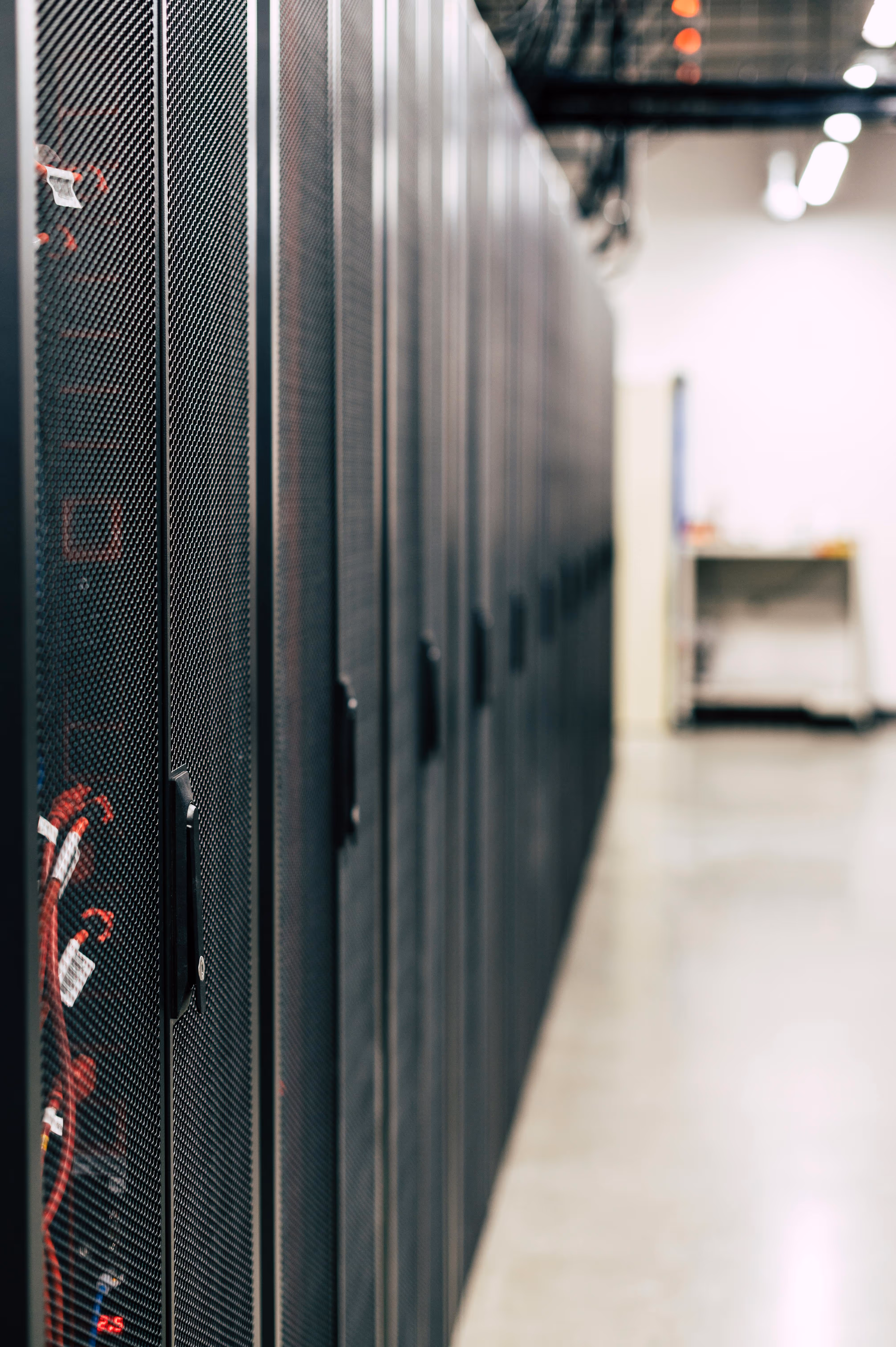 A row of black server racks with visible red network cables inside, in a data center with a blurred background.