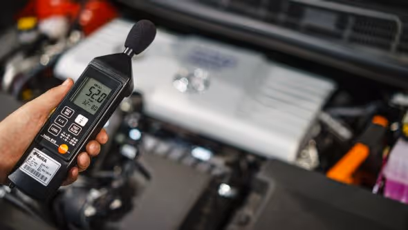 Hand holding a sound level meter near equipment.