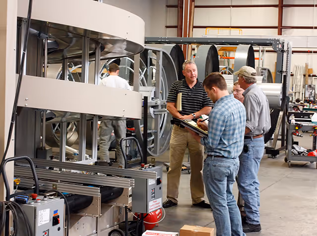 Four men in a factory setting discussing near large industrial machinery with spiral components.