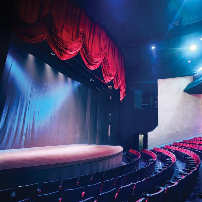 Empty theater with a curved stage under red curtains and rows of red and black seats.