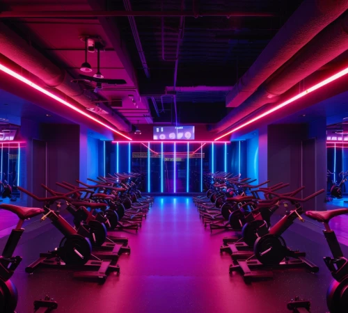 Indoor cycling studio with rows of stationary bikes under purple and blue neon lighting.