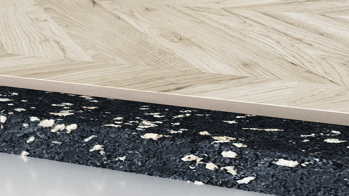 Close-up of a light wood patterned vinyl plank resting on a textured black and white underlayment.