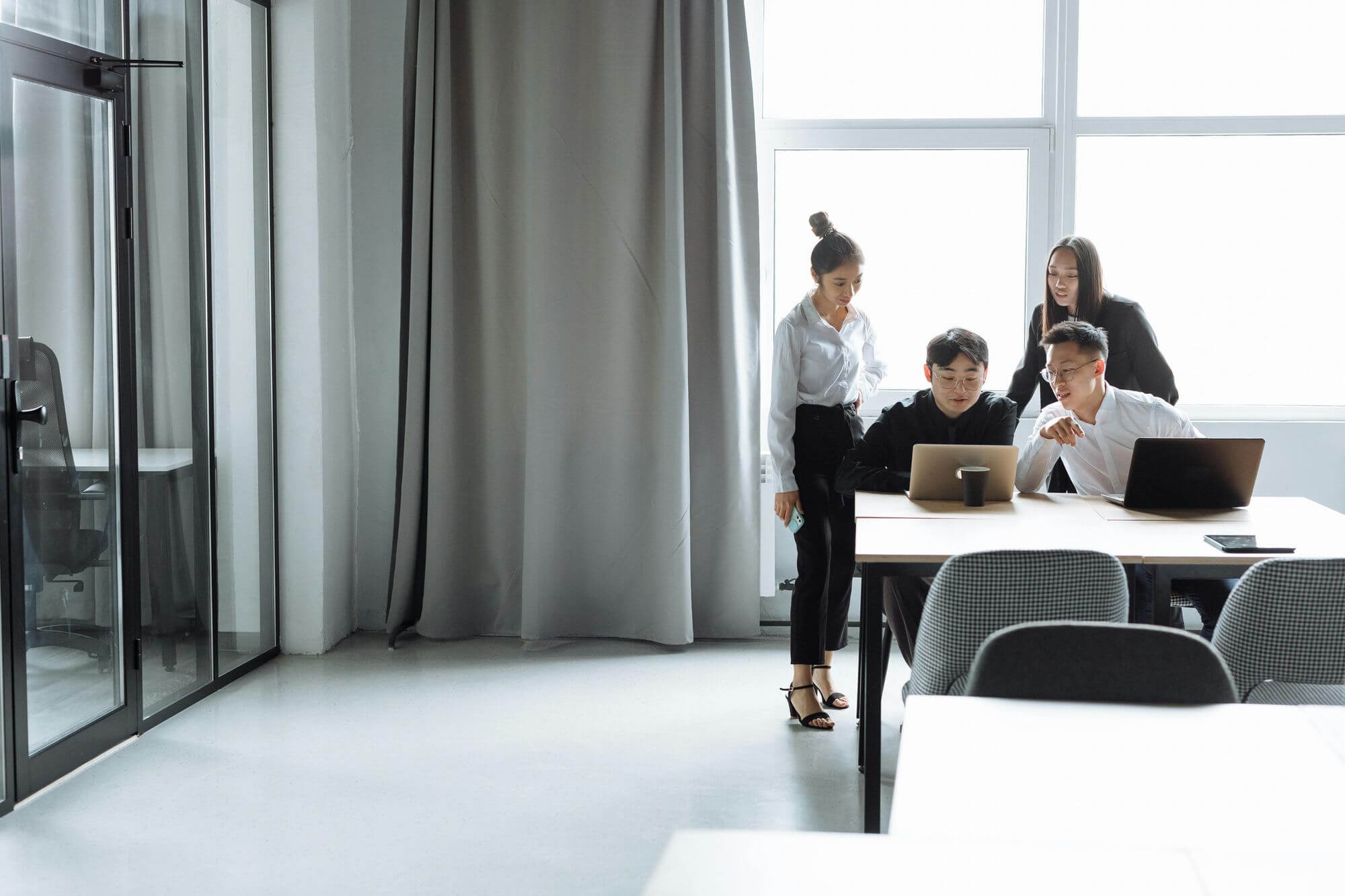 Four young professionals collaborating around a table with laptops in a bright modern office.