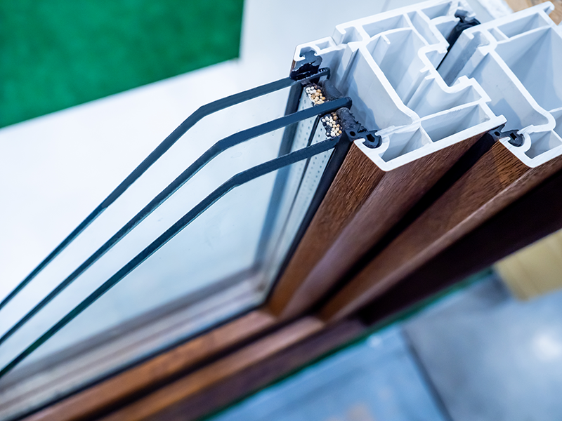 Close-up of a triple-pane insulated glass window with a wood-colored frame and white internal structure.