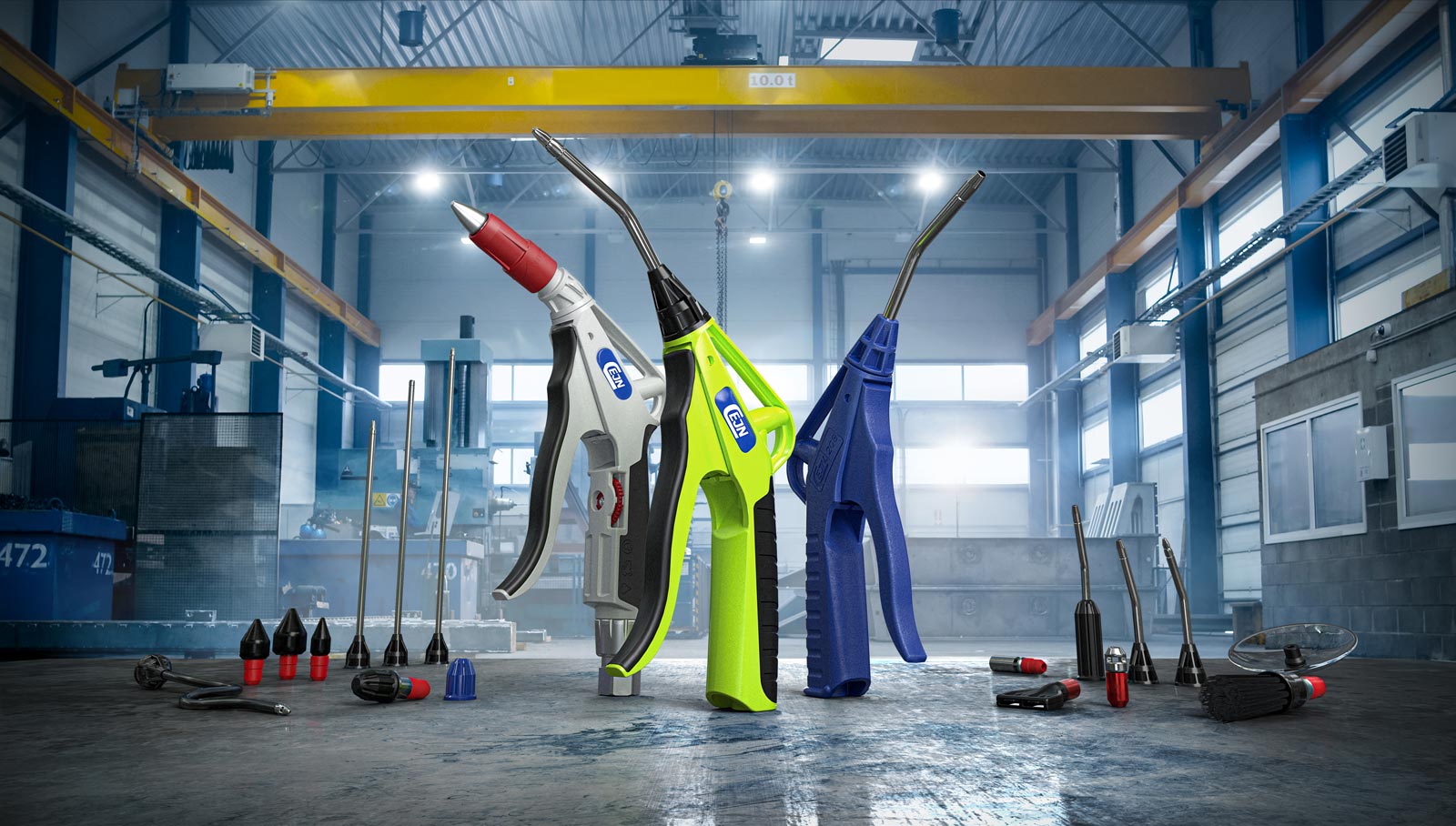 Three industrial air blow guns in red, green, and blue, surrounded by various nozzle attachments on a factory floor.