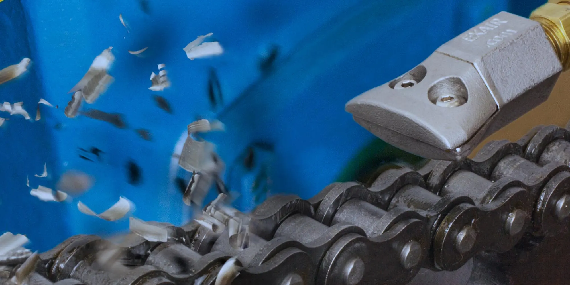 Metal tool shaving wood while cutting along a metal chain with wood chips flying.