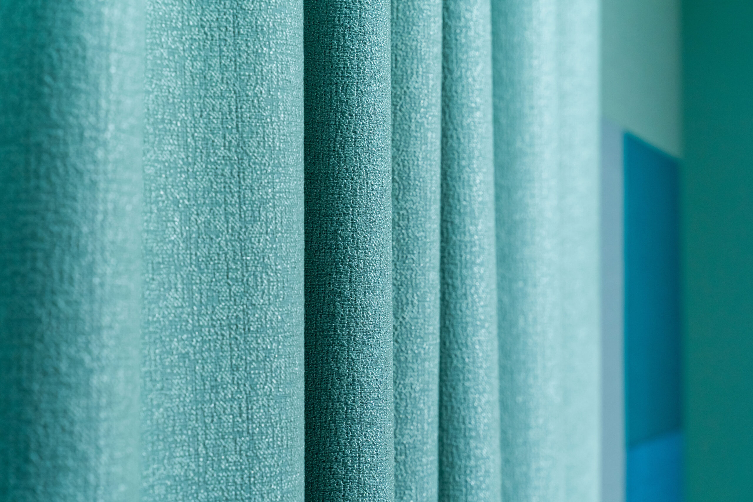 Close-up view of textured turquoise fabric curtains with soft folds and a blurred wall background.