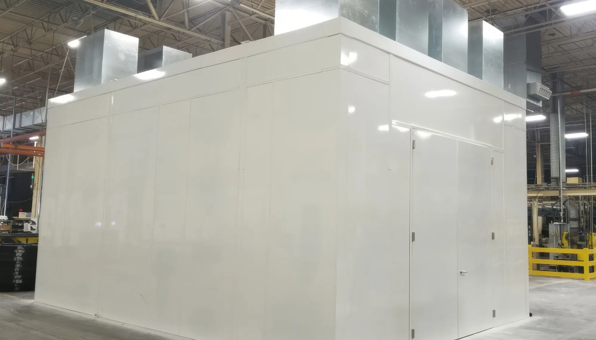 Large white industrial enclosure with ventilation ducts on top inside a warehouse.