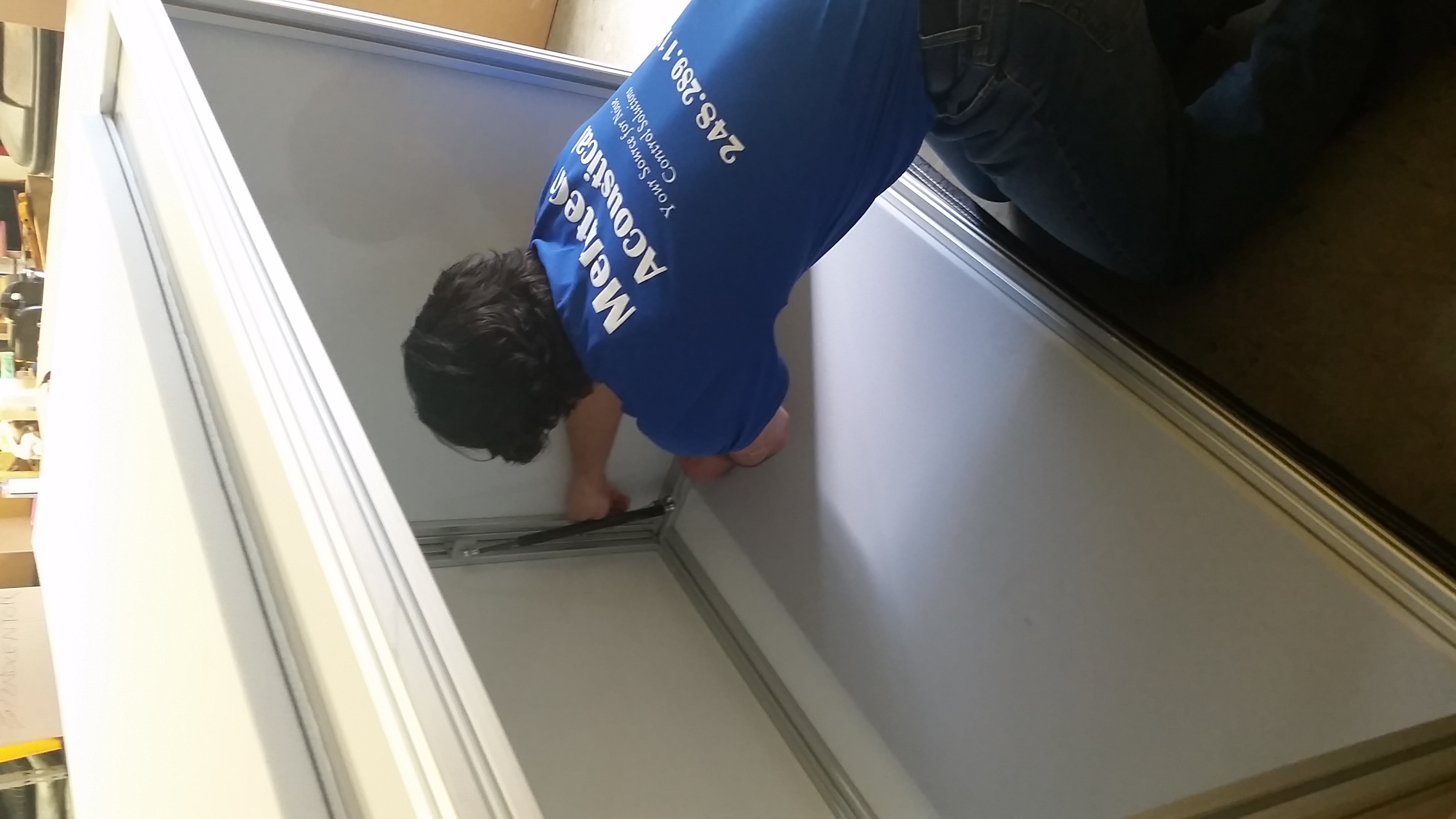 Person wearing a blue shirt with 'MeriTech Acoustical' text, working inside a large white industrial or storage cabinet.