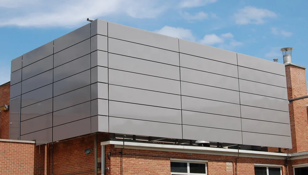 Building extension with smooth gray metal panels installed above a brick structure under a partly cloudy sky.