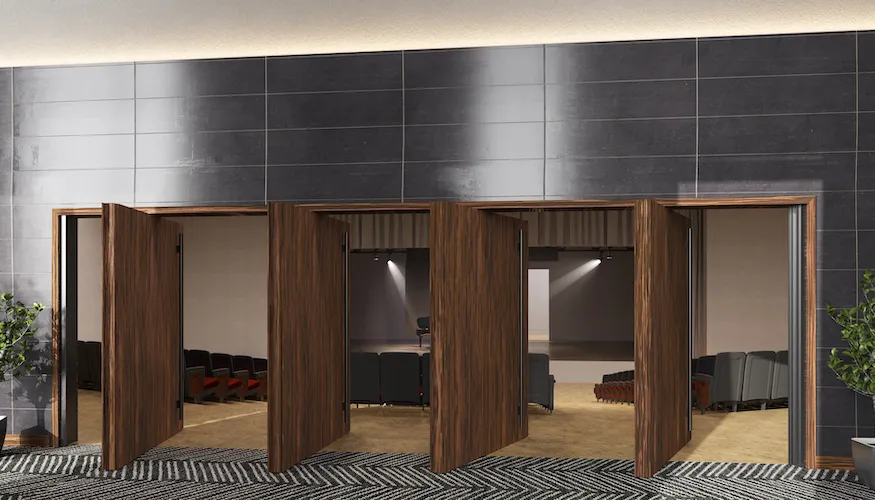 Wooden acoustic pivot doors partially open revealing a theater with seats and stage lighting.