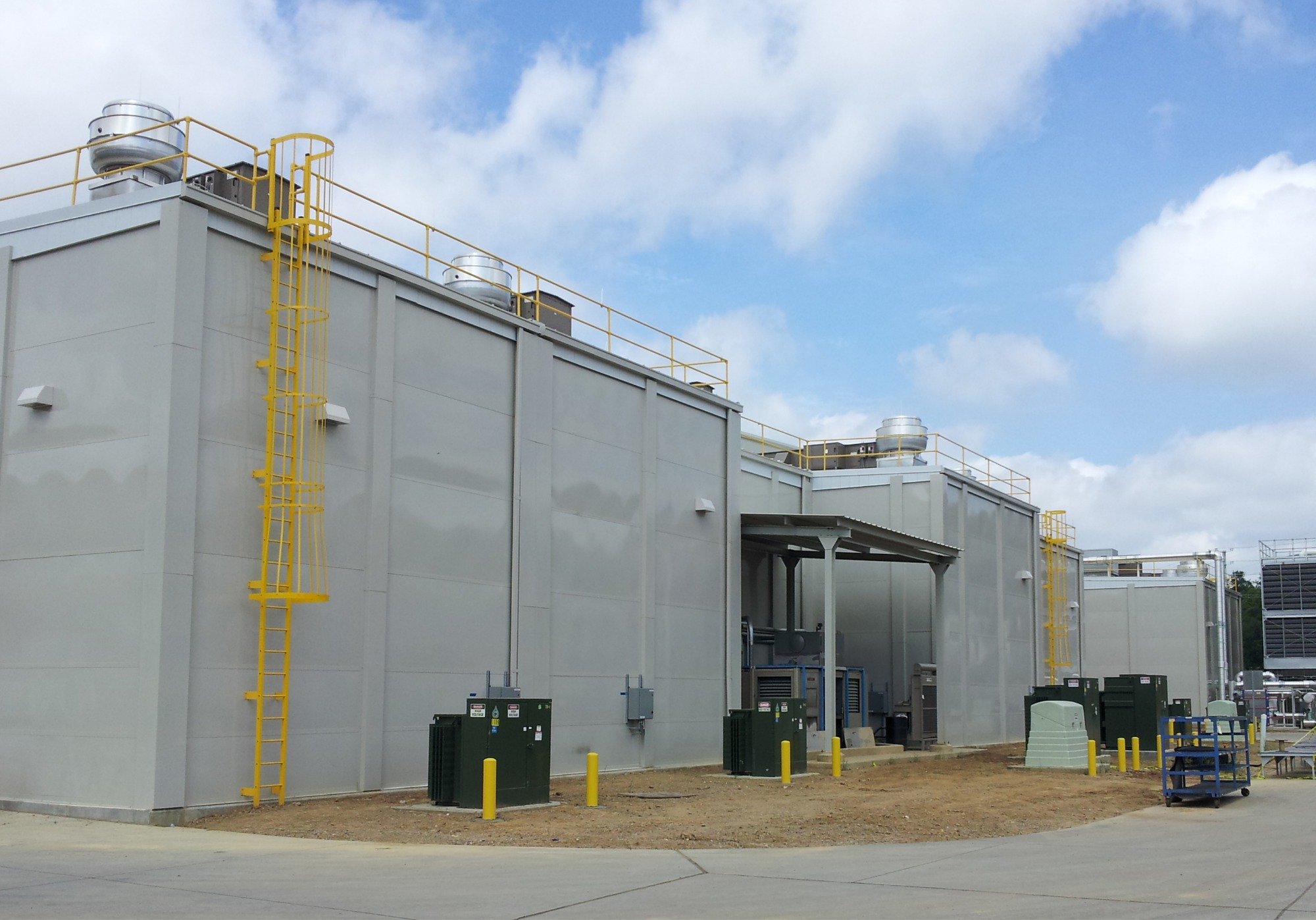 Tall modular acoustic barrier wall panels enclosing outdoor mechanical equipment and cooling towers.