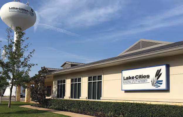 Exterior of the Lake Cities Municipal Utility Authority building with branded signage and a nearby water tower on a sunny day