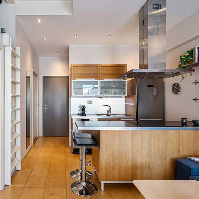 Kitchen remodel in Chicago with wooden cabinets, stainless steel appliances, two black bar stools, and a gray door in the background.