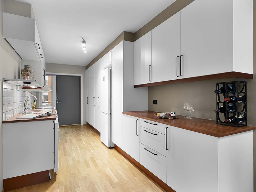 Modern galley kitchen remodel in New York with white cabinets, wooden countertops, hardwood floor, and a wine rack with bottles.