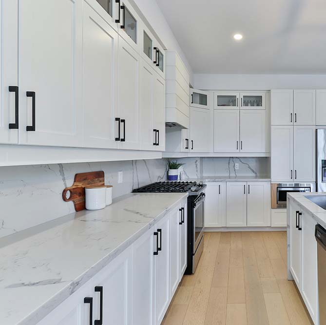 Kitchen remodel in Houston with white cabinetry, black handles, marble countertops, and light wooden floors.